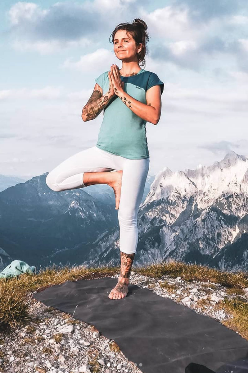 teacher Romana Schwaiger practicing a yoga pose at the top of a mountain